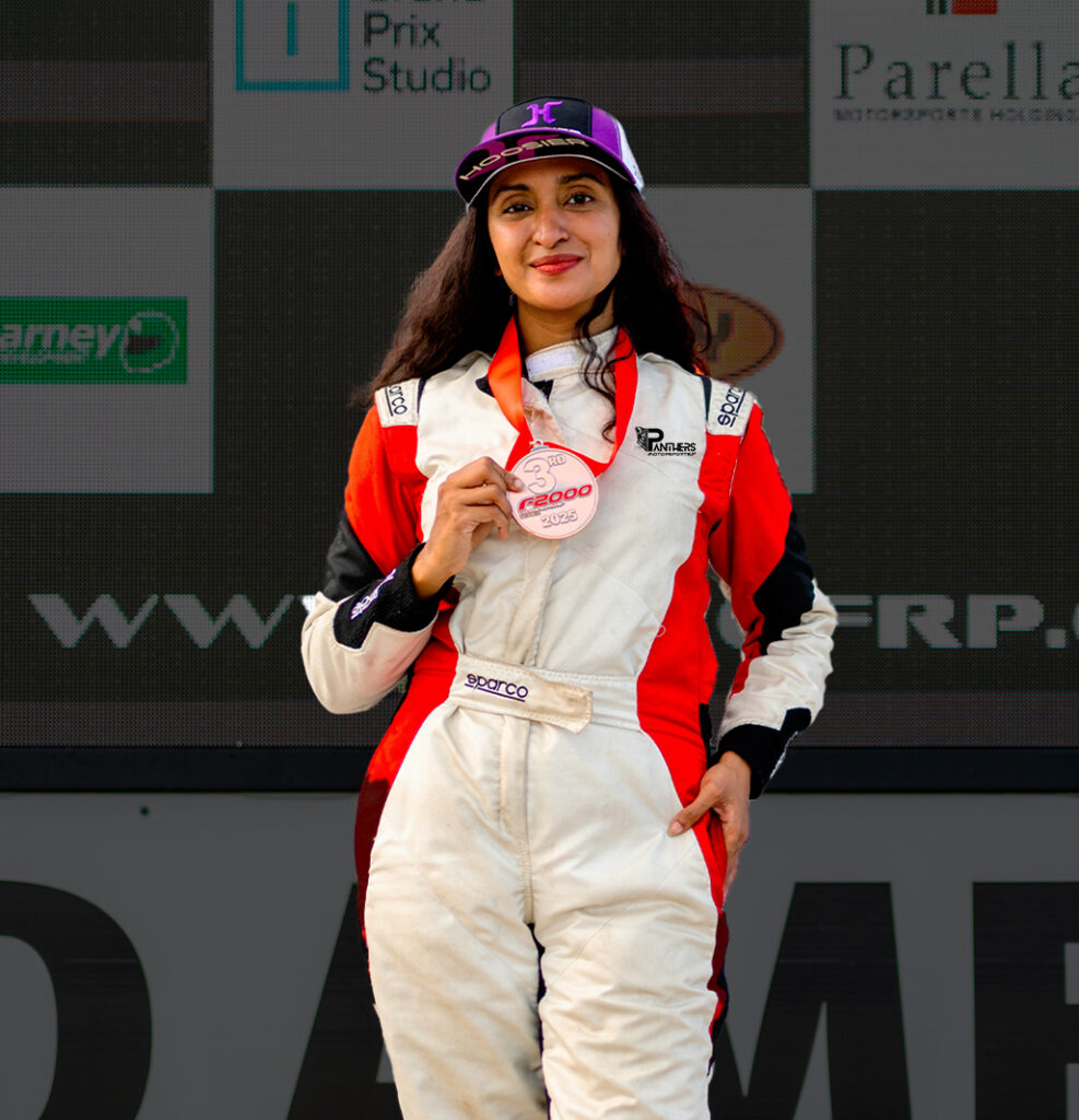 Female race driver holding a third-place podium medal at the track