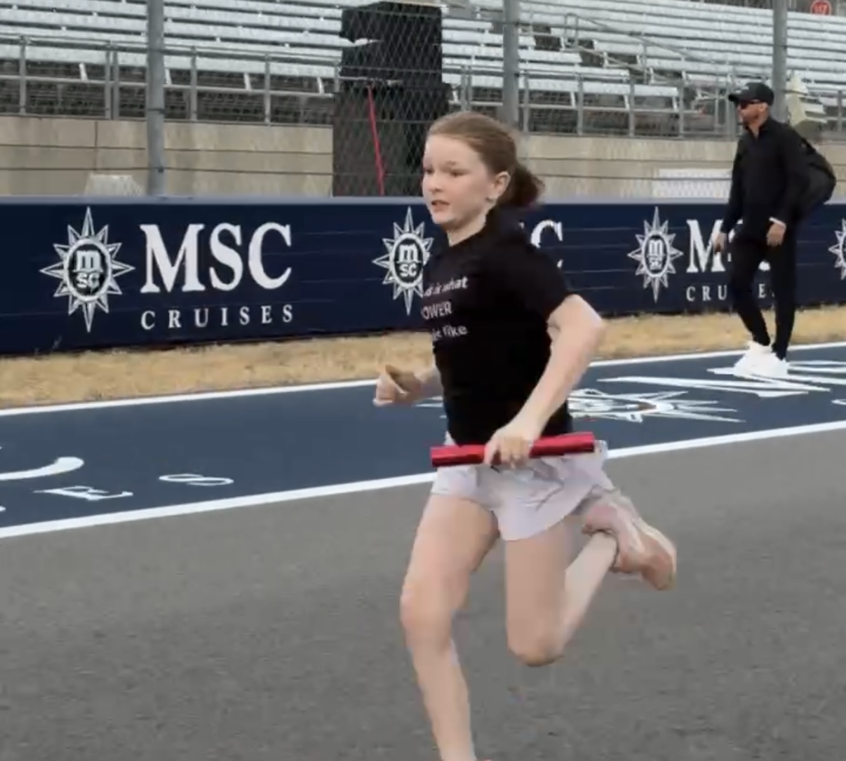 Young girl sprinting with a relay baton down the COTA pit straight
